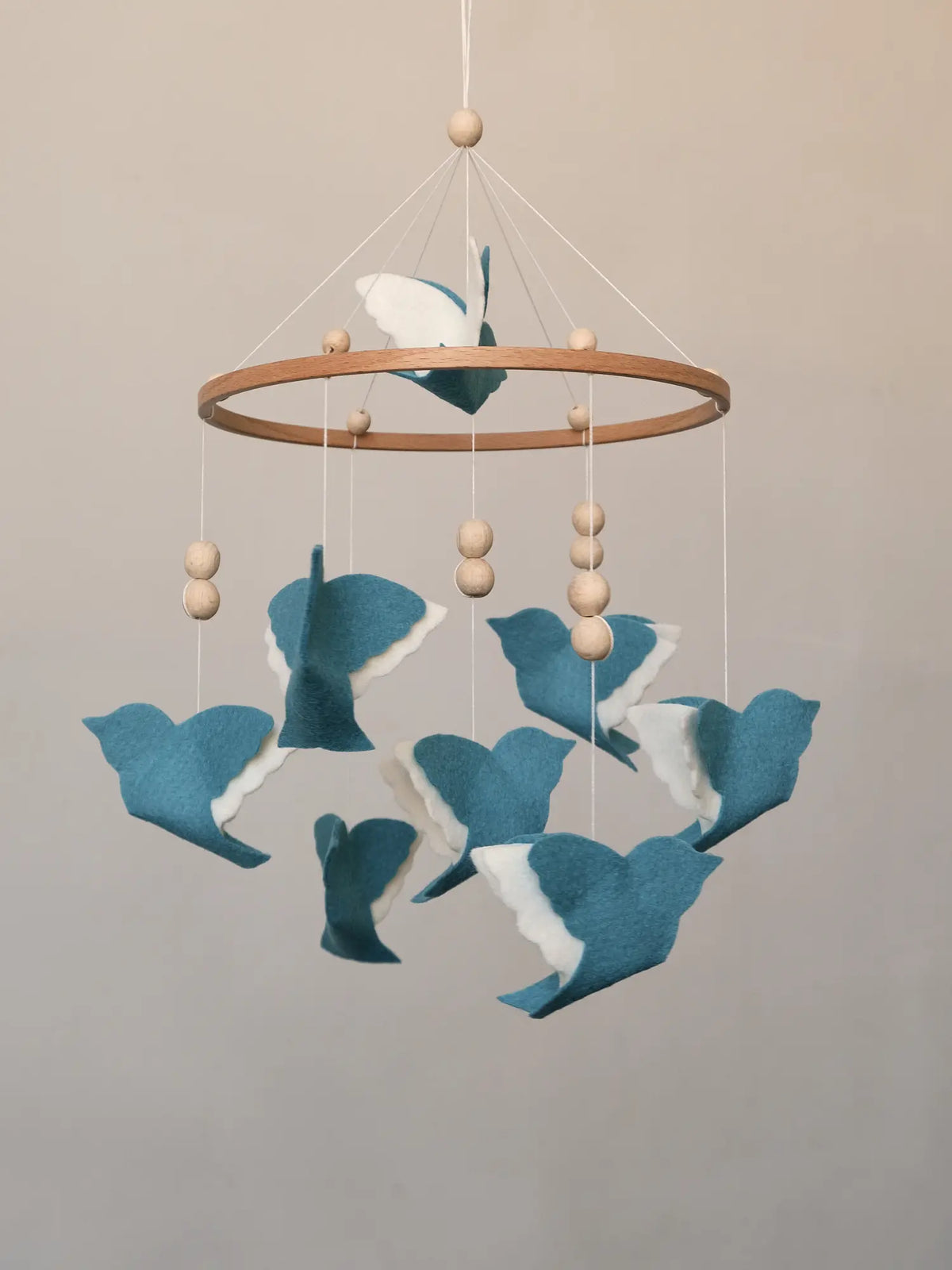 Blue felt bird baby mobile with layered white wings, wooden hoop and natural wood beads, front view