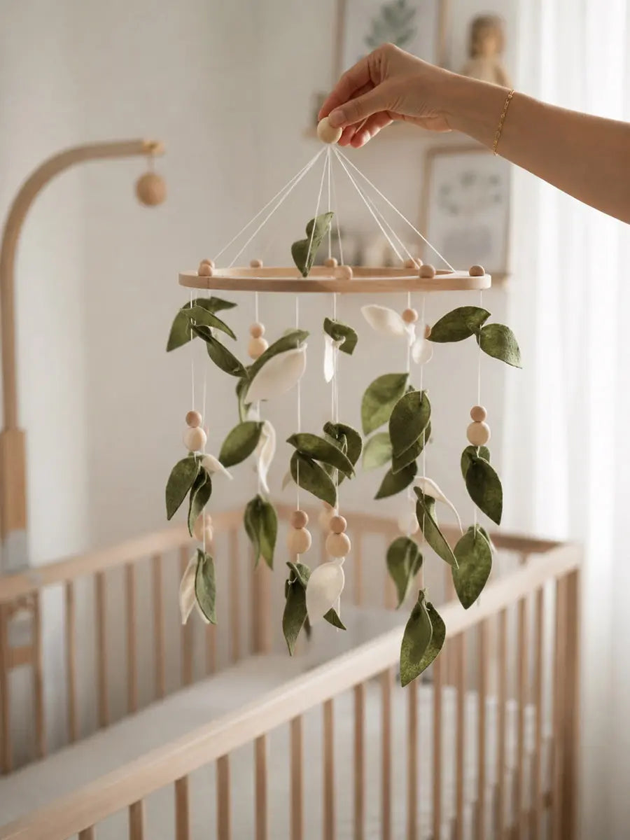 Handmade baby mobile with green felt leaves and wooden beads hanging above nursery crib
