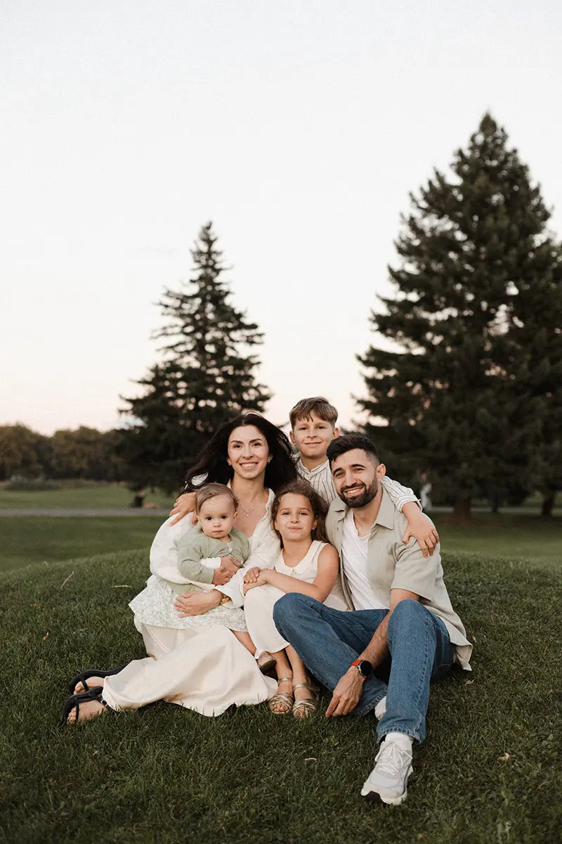 Alina and her family sitting together on the grass with trees behind them