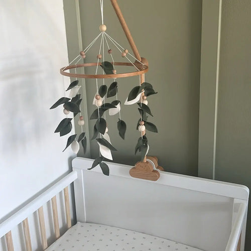Green leaves felt mobile on wooden arm above white crib – boho nursery decor with olive green wall