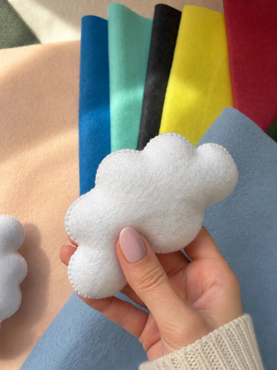 Handmade felt cloud for baby mobile held in hand with colorful felt fabric swatches