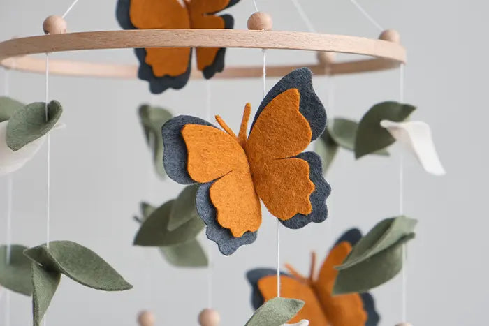 Handmade monarch butterfly felt baby mobile close-up – orange and navy blue butterflies with green eucalyptus leaves