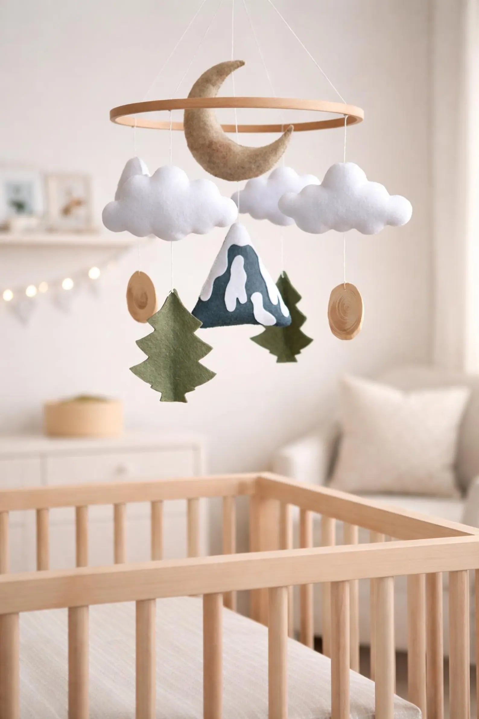 Felt mountain moon mobile above crib in nursery – woodland baby room decor with fairy lights