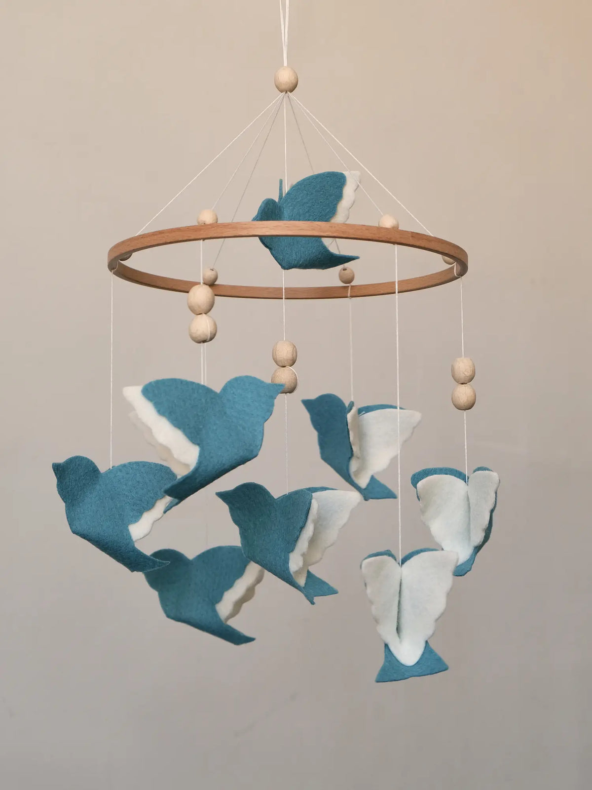 Blue flying bird mobile with layered white wings and wooden beads shown from the side
