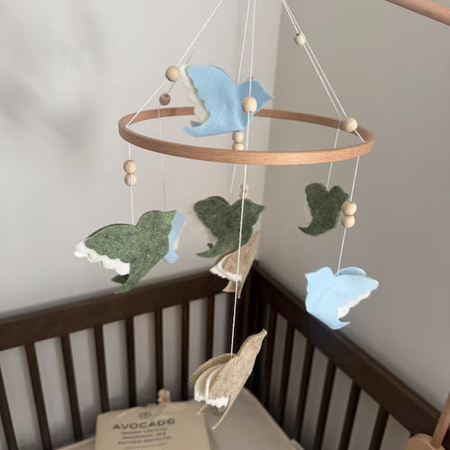 Customer photo of a custom felt bird baby mobile in blue, green and beige above a dark wooden crib