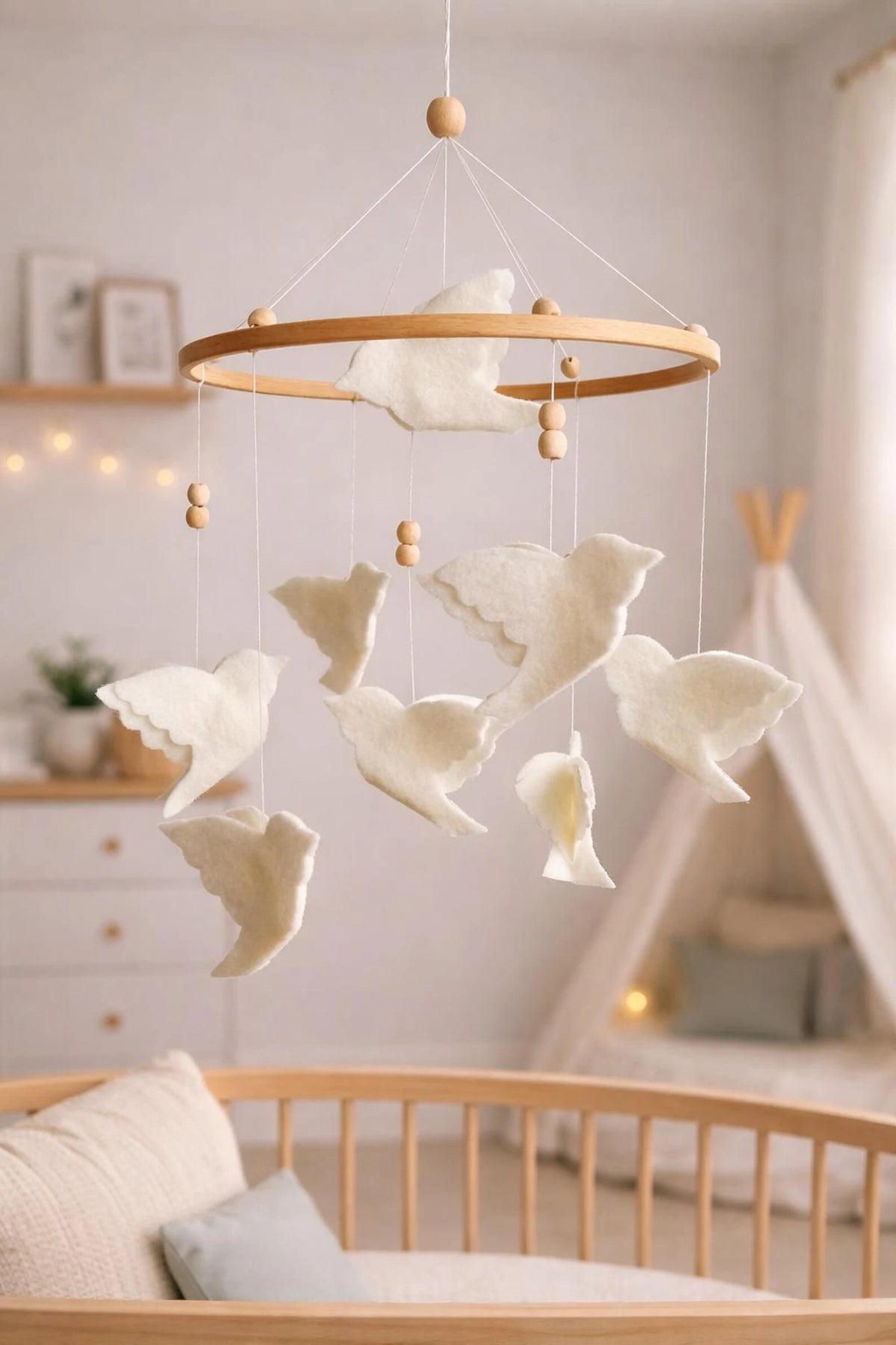 White flying bird crib mobile on a wooden hoop in a soft neutral nursery with a play tent