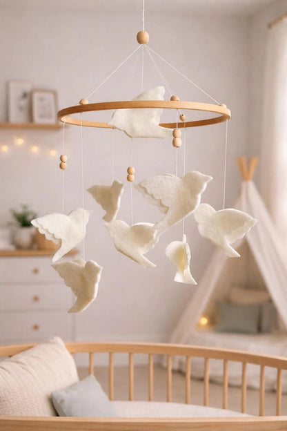 White flying bird crib mobile on a wooden hoop in a soft neutral nursery with a play tent