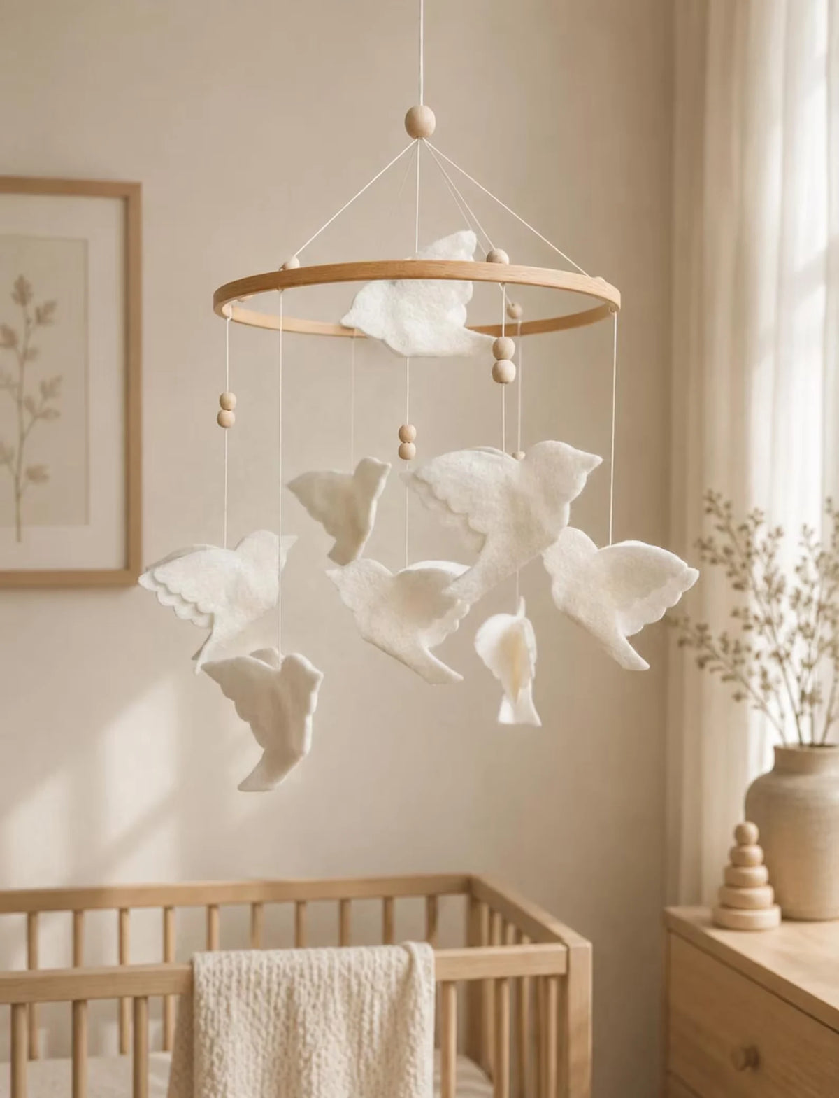 White felt bird mobile with layered flying birds and wood beads hanging above a natural wooden crib