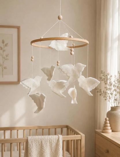 White felt bird mobile with layered flying birds and wood beads hanging above a natural wooden crib