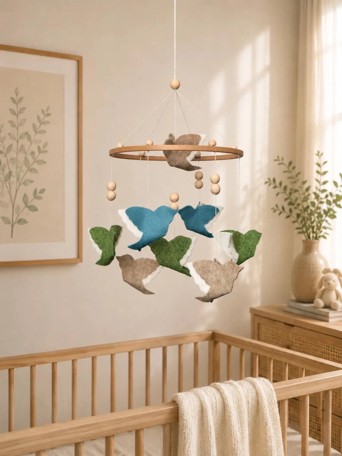 Woodland Mix felt bird baby mobile with blue, green and beige flying birds above a wooden crib