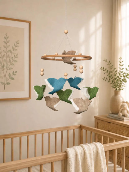 Woodland Mix felt bird baby mobile with blue, green and beige flying birds above a wooden crib