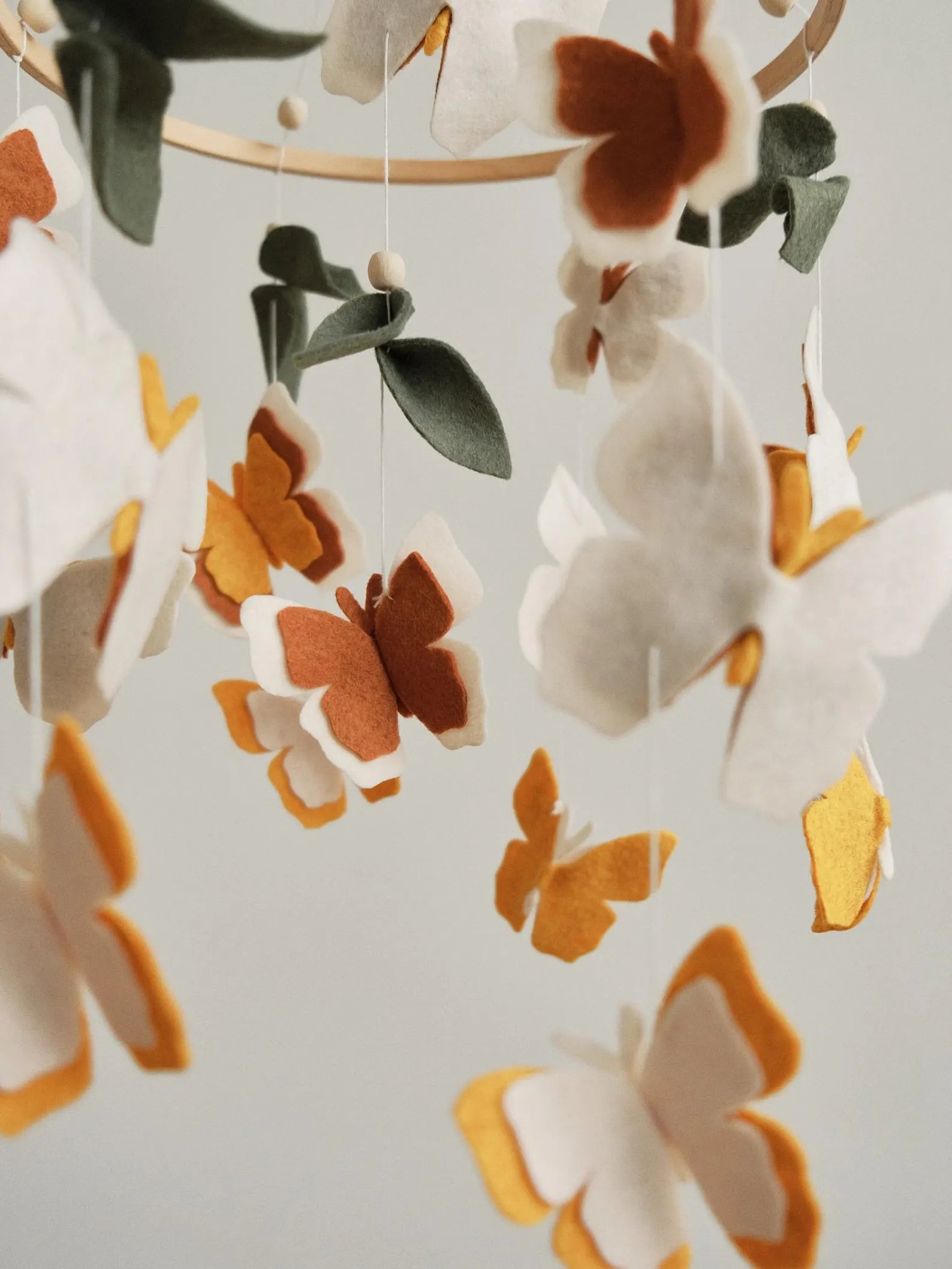 Felt butterfly mobile closeup – amber, terracotta and cream layered wings with sage green leaves