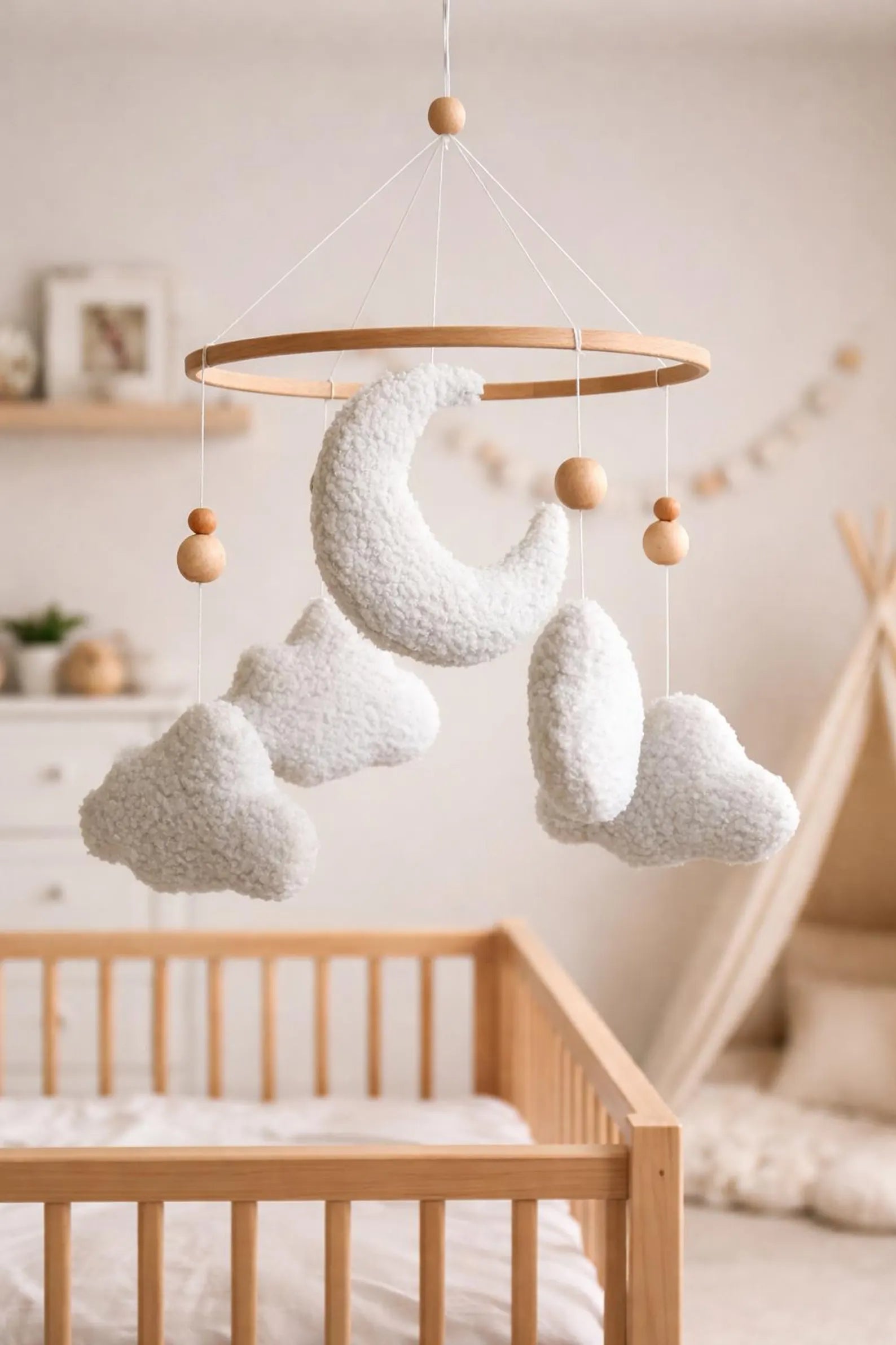 Soft boucle cloud and moon mobile hanging above wooden crib in neutral nursery with teepee