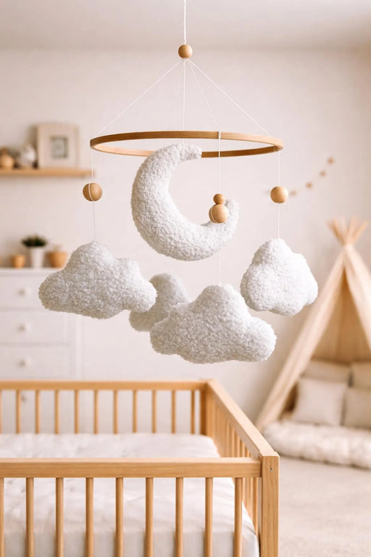 White plush baby mobile with boucle moon and clouds above crib in cozy nursery