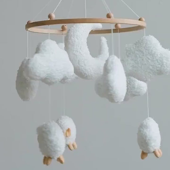 Soft boucle baby mobile with sheep and clouds gently spinning above nursery crib