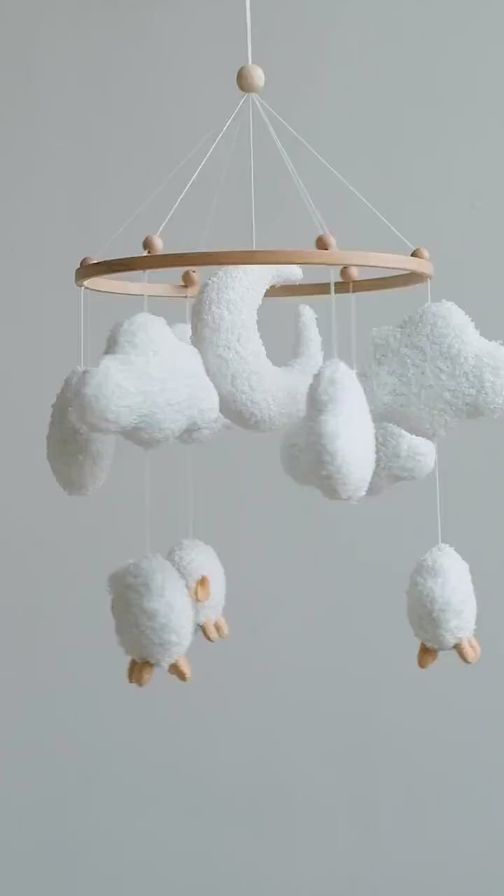 Soft boucle baby mobile with sheep and clouds gently spinning above nursery crib