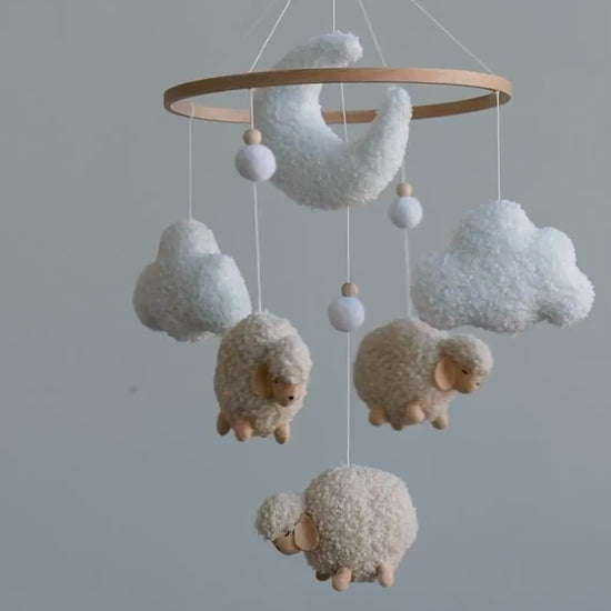 Handmade boucle sheep moon and cloud baby mobile slowly spinning above nursery crib