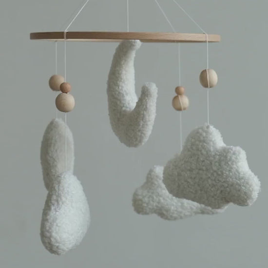 Handmade boucle baby mobile with moon and clouds gently spinning above nursery crib