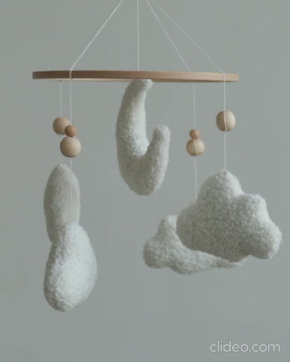 Handmade boucle baby mobile with moon and clouds gently spinning above nursery crib