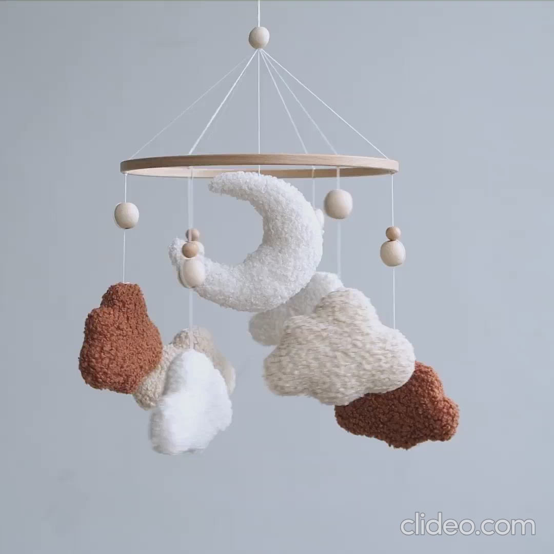 Handmade boucle baby mobile with terracotta and cream clouds spinning above crib
