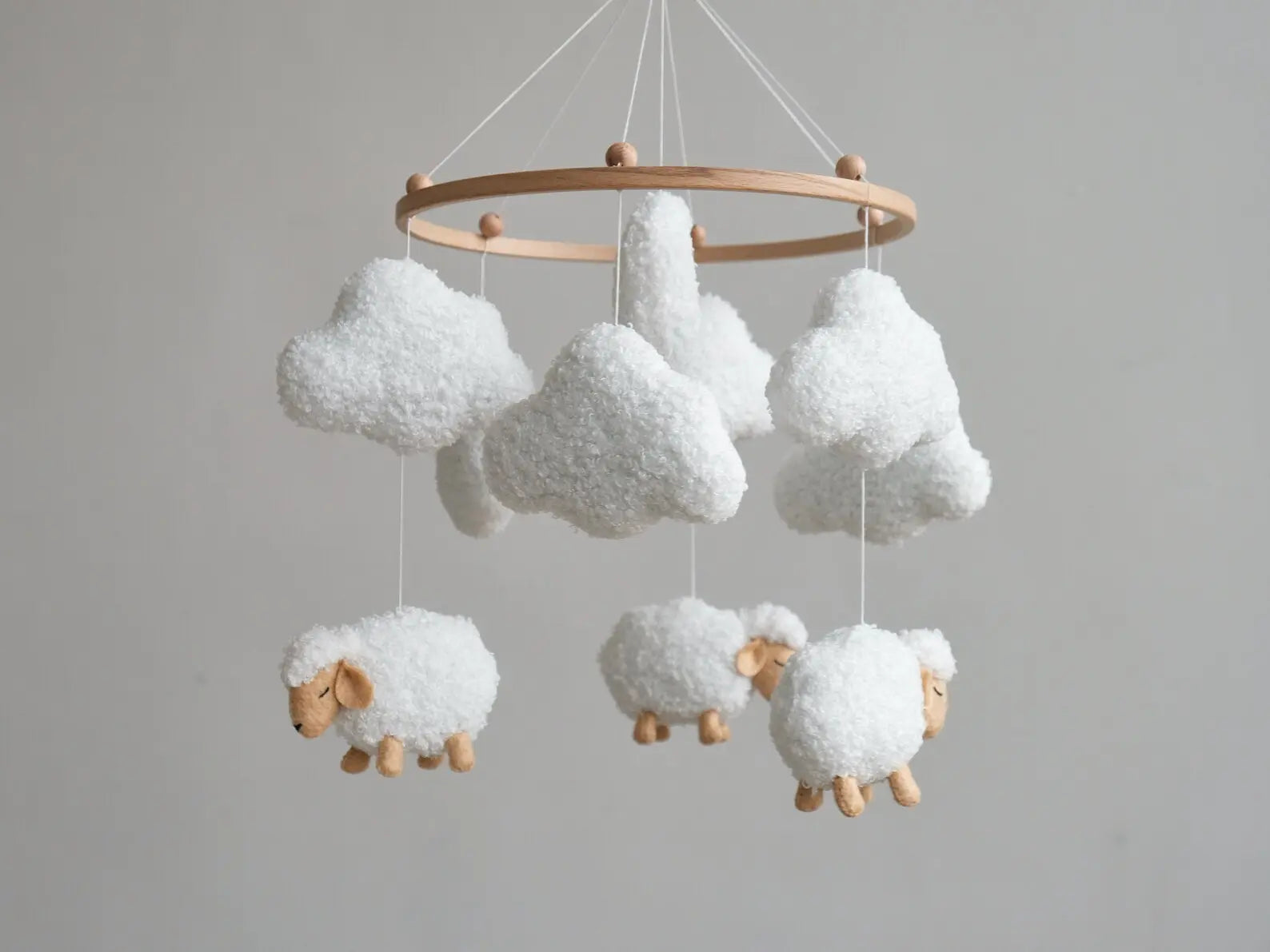 Hand holding white boucle cloud from soft baby mobile with sheep and clouds in background