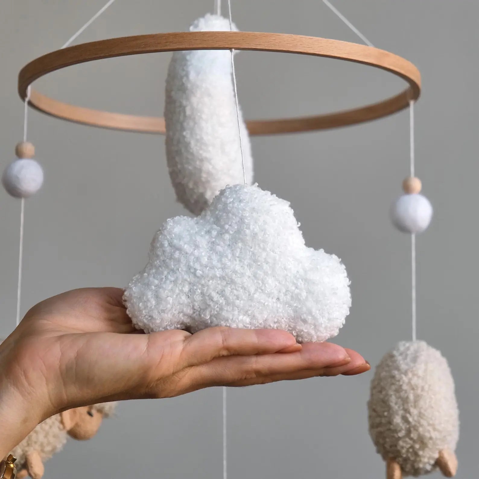 Handmade white boucle cloud held in hand with sheep baby mobile in background