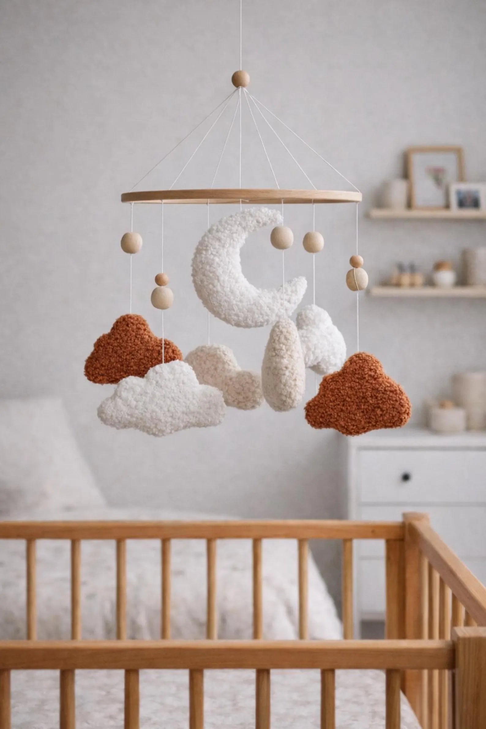 Boucle terracotta cloud baby mobile hanging above wooden crib in neutral nursery