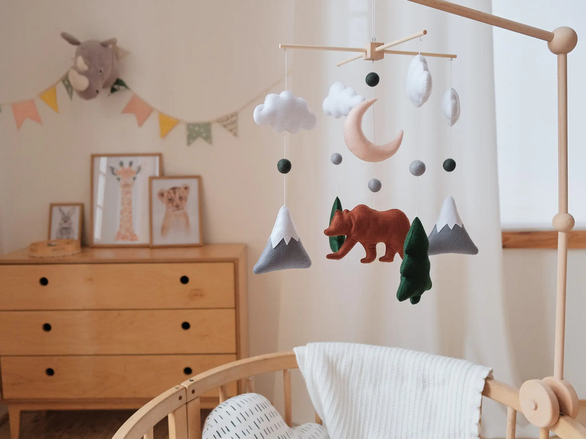 Woodland crib mobile with felt bear, clouds, moon and mountains above a wooden crib in a nursery