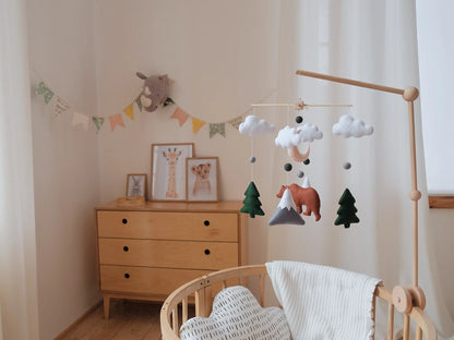 Woodland nursery mobile with a brown felt bear, snowy mountains, fir trees and clouds above crib